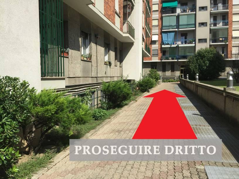 Cortile interno con edificio sullo sfondo, freccia che indica di continuare dritto